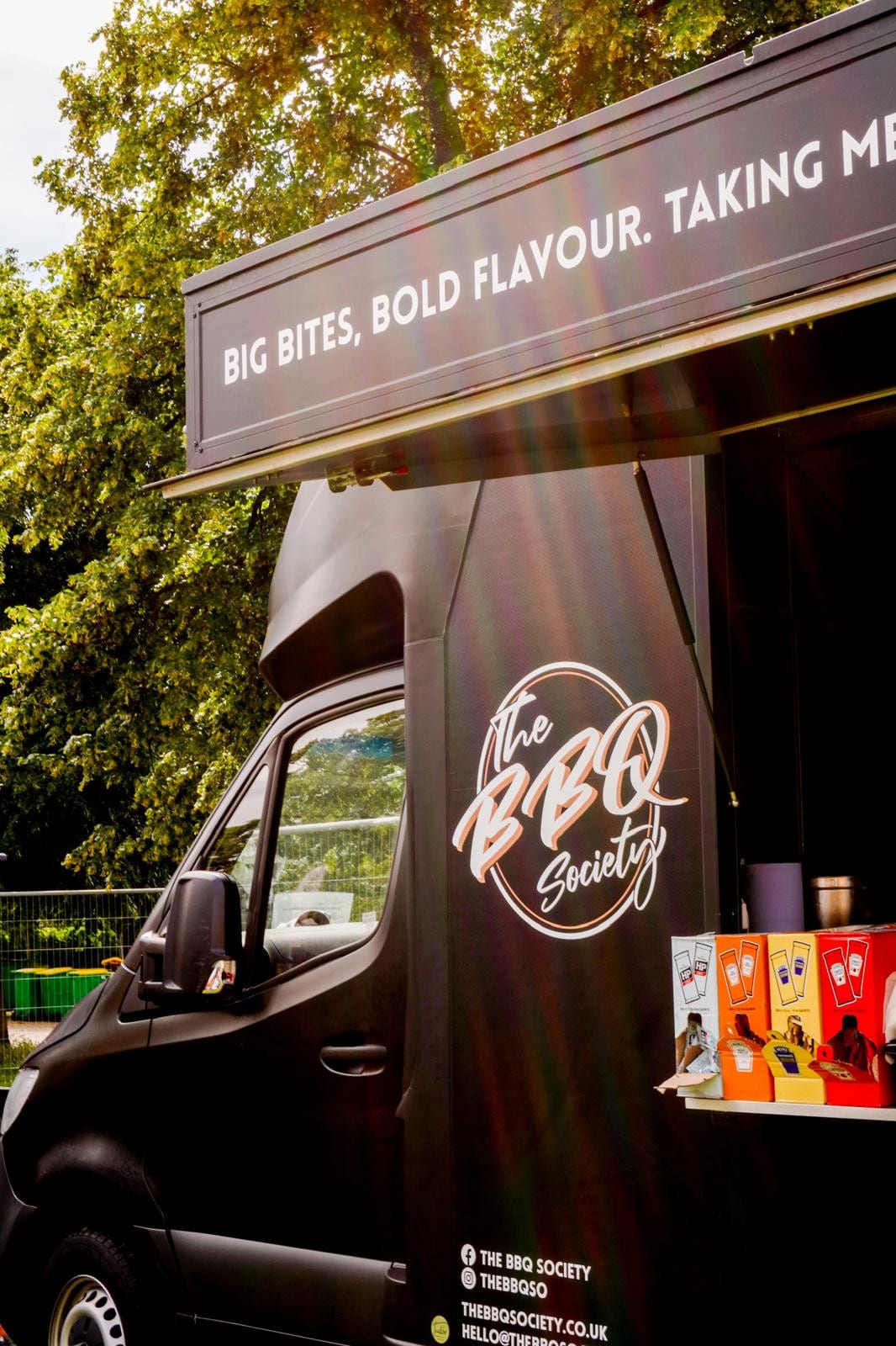 The BBQ Society's black catering van with its serving hatch open at an outdoor event