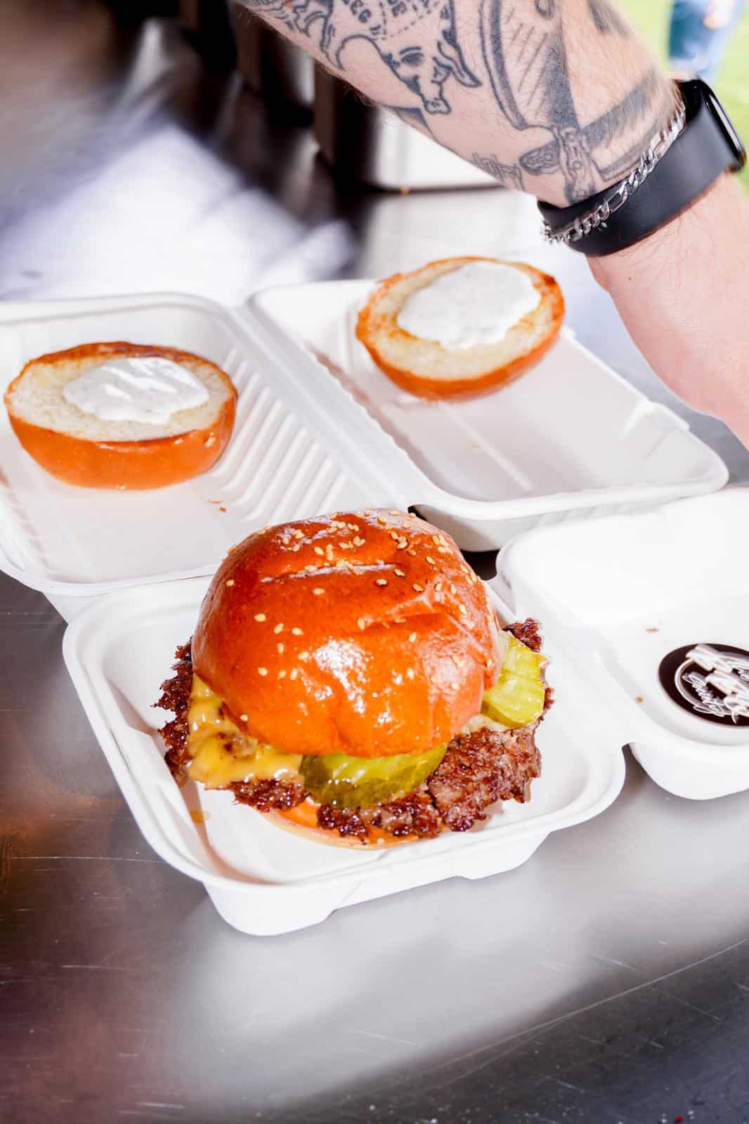 A smash burger with melted cheese and pickles in a sesame brioche bun, served by The BBQ Society